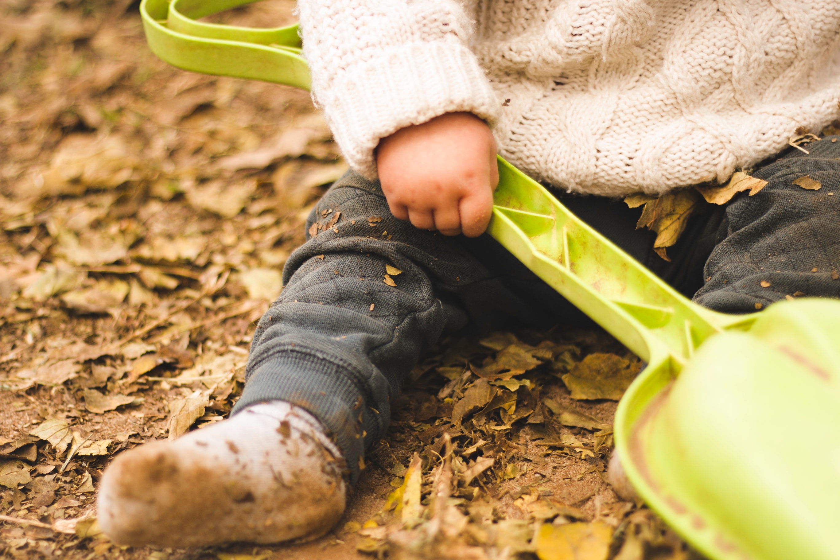 image of toddler's hand while sitting in leaves with shovel