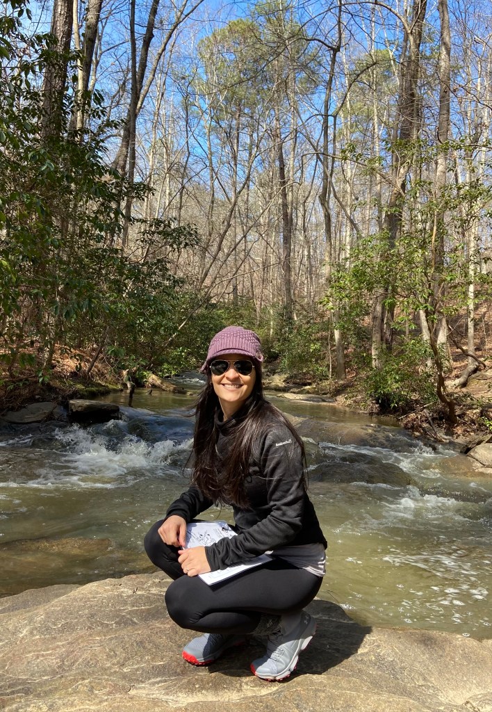 Glo Perez, kneeling on a rock in front of a river.
